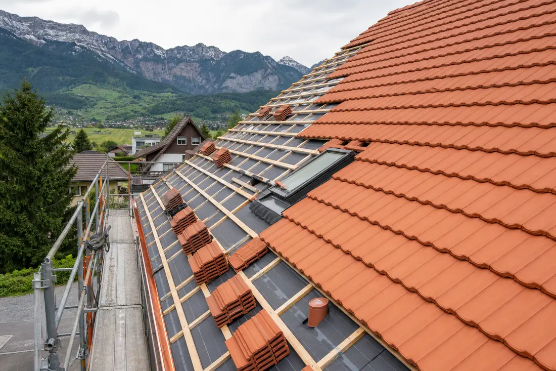 Chantier de rénovation de toiture avec pose de tuiles neuves sur une maison romande